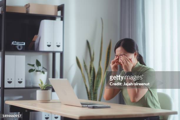 mujer asiática que sufre de dolor en los ojos sentada en la oficina de casa. - bloodshot fotografías e imágenes de stock
