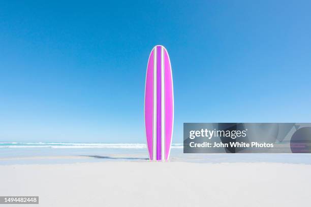 pink and purple retro surfboard on an empty beach. waves in the background. blue sky with copy space. - idyllic surfboard stock pictures, royalty-free photos & images