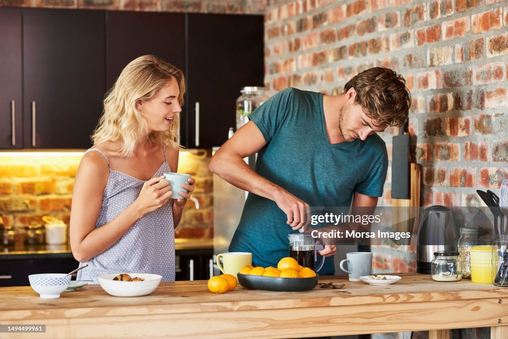 Woman looking at man preparing coffee in kitchen
