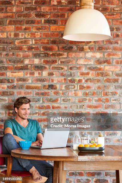 young man working on laptop at table by brick wall - table brick wall wood stock-fotos und bilder