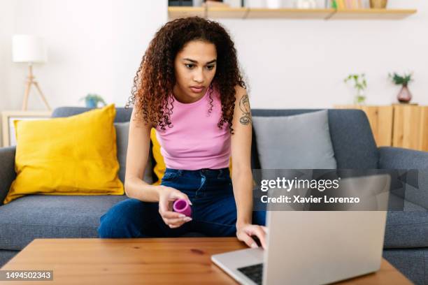 latin american teenage girl holding menstrual cup looking for use instructions browsing on laptop computer at home. feminine hygiene lifestyle and millennial people generation concept - tampon stock pictures, royalty-free photos & images