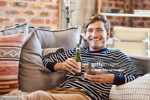 happy man holding smart phone and beer bottle - zurücklehnen stock-fotos und bilder
