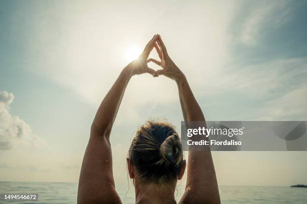 portrait of a woman with outstretched arms standing in a swimsuit in the ocean, view from the back - welcome back stock-fotos und bilder