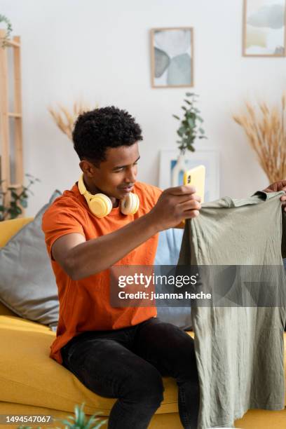 side view of african american male sitting on sofa checking some clothes - facing things head on stock pictures, royalty-free photos & images