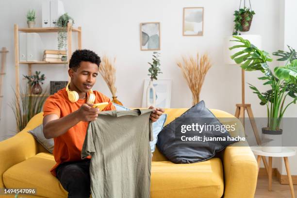 side view of african american male sitting on sofa checking some clothes - facing things head on stock pictures, royalty-free photos & images