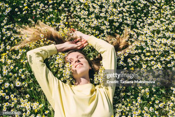 a young woman in a yellow sweater lies in a field of daisies, top view. - frau blumenwiese stock-fotos und bilder