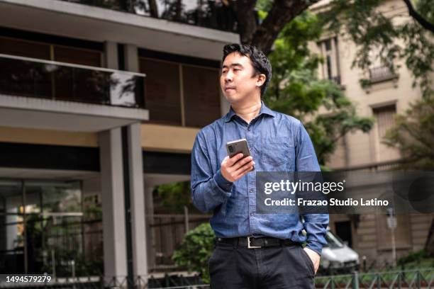 mid adult man looking around while using mobile phone in the city - uber in buenos aires argentina stock pictures, royalty-free photos & images