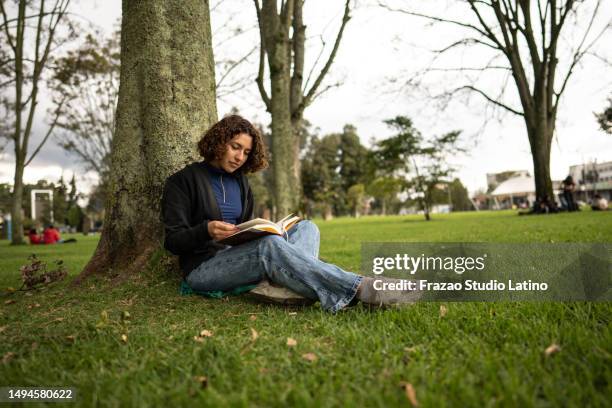 mujer joven leyendo un libro en el parque - mujer leyendo libro en el parque fotografías e imágenes de stock