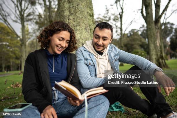 young couple reading a book in the public park - south american people stock pictures, royalty-free photos & images