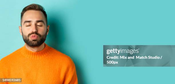 close-up of young man in sweater pucker lips,close eyes and waiting - hipster beard plain background stock-fotos und bilder