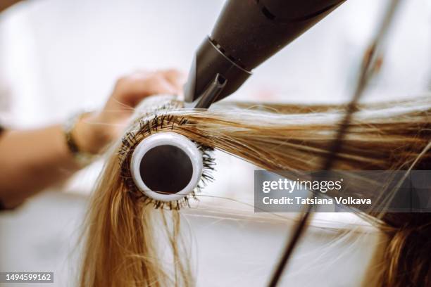 close-up view of lock of long blond hair on hairbrush being dried by blow dryer - salone di parrucchiere foto e immagini stock