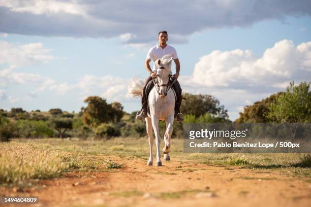 young male riding white horse in grassy meadow on cloudy day in countryside,spain - horse and male and riding foto e immagini stock