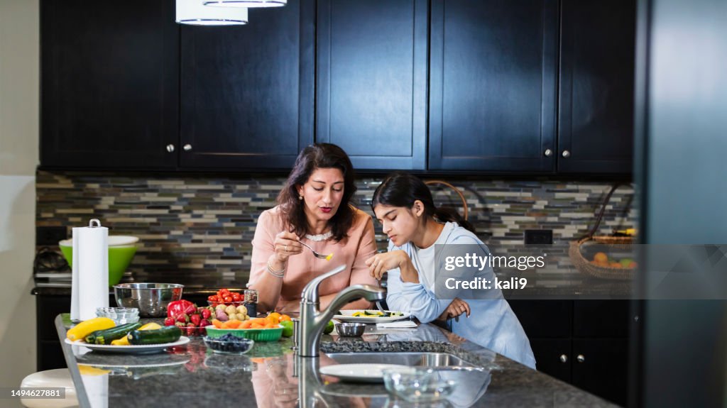 Asian mother, teenage daughter talk and eat in kitchen