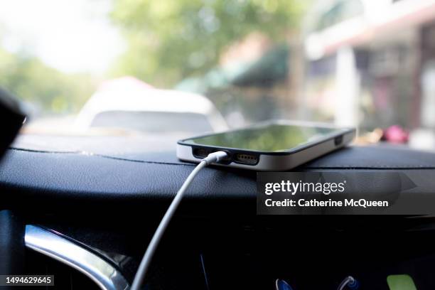 smart phone charging battery while on car dashboard - cargador de móvil fotografías e imágenes de stock