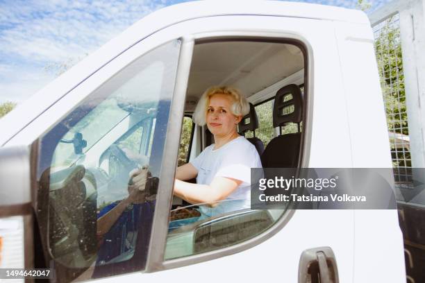 mature semi-truck driver in white t-shirt sitting at driver seat of big truck delivering goods - truck side view stock pictures, royalty-free photos & images