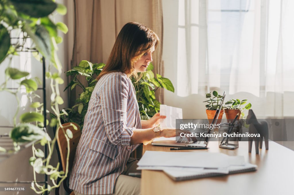 Top view close up woman calculating bills, money, loan or rent payments, using laptop, online banking service, sitting at table, female holding receipt, planning budget, managing expenses, finances