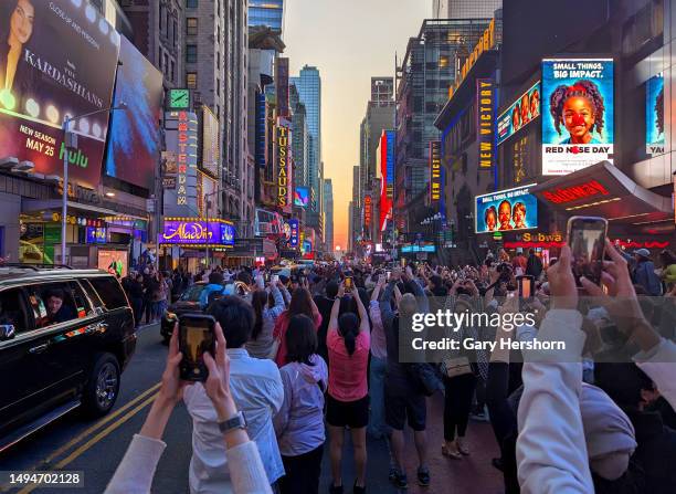 People stand on 42nd Street in Times Square as they photograph the second evening of the Manhattanhenge sunset on May 30 in New York City.