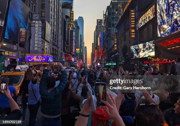 People stand on 42nd Street in Times Square as they photograph the second evening of the Manhattanhenge sunset on May 30 in New York City.