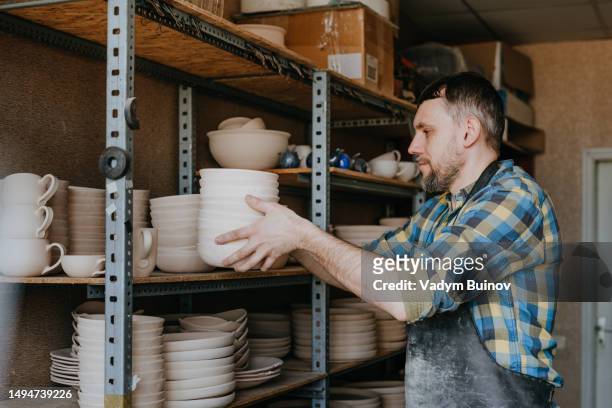 potter putting raw clay dishes on the shelf in a workshop. side view, selective focus. - kinetic sculpture stock pictures, royalty-free photos & images