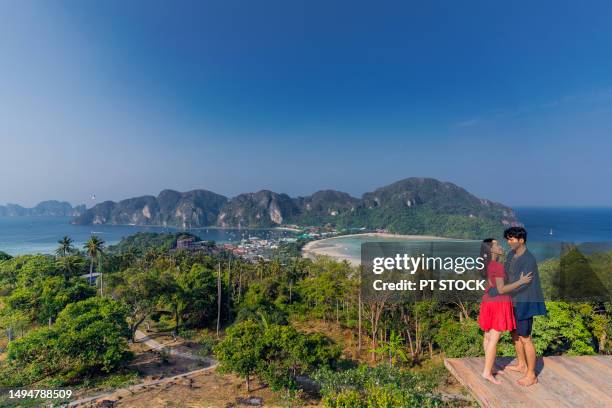 a man and a woman stand at the view point of koh phi phi. view of mountains below and buildings, sea and boats at koh phi phi, krabi province, thailand. - phuket province stock-fotos und bilder