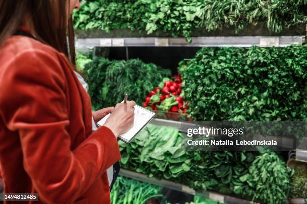 woman making notes in notebook at counter with fresh vegetables and herbs in store - borough market stock pictures, royalty-free photos & images