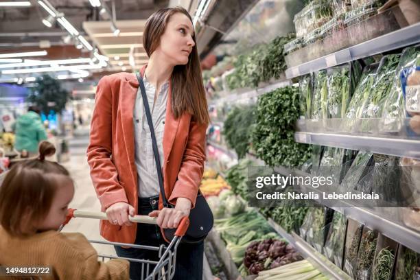 mindful nutrition: mother and child attentively examining the array of fresh greens on the shelves, embracing the concept of mindful eating and the vital role of vitamins in their diet. - madre ama de casa fotografías e imágenes de stock