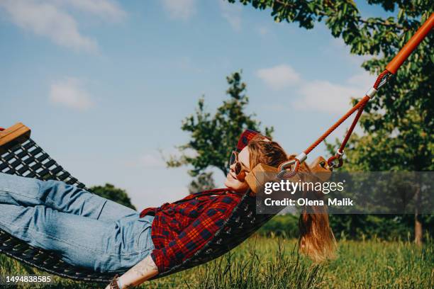 redhead woman relaxing in hammock outdoors. beautiful green field - hannover fotografías e imágenes de stock