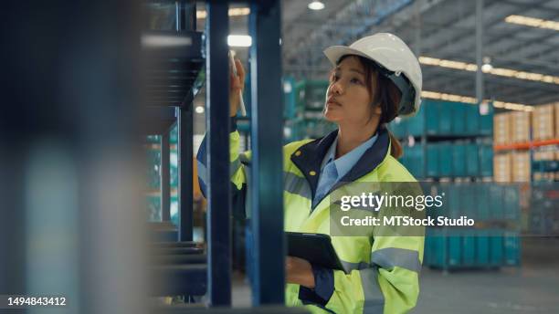 young asian woman warehouse worker checks stock and inventory with digital tablet in factory warehouse. logistic industry business. - electronic products stockfoto's en -beelden