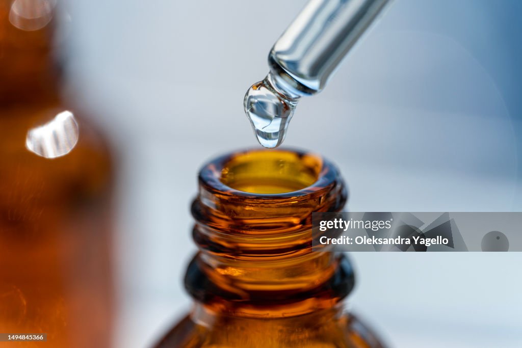 Open amber bottle dropper pipette with serum or essential oil. Container with cosmetic transparent liquid.