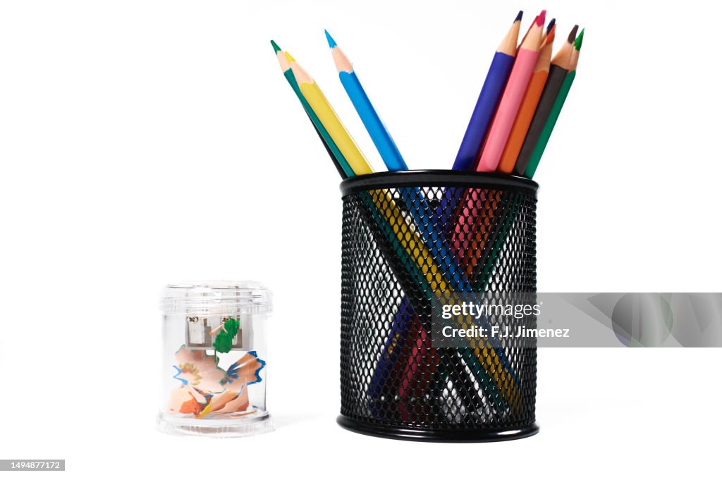 Colored pencils in pen holder and sharpener on white background