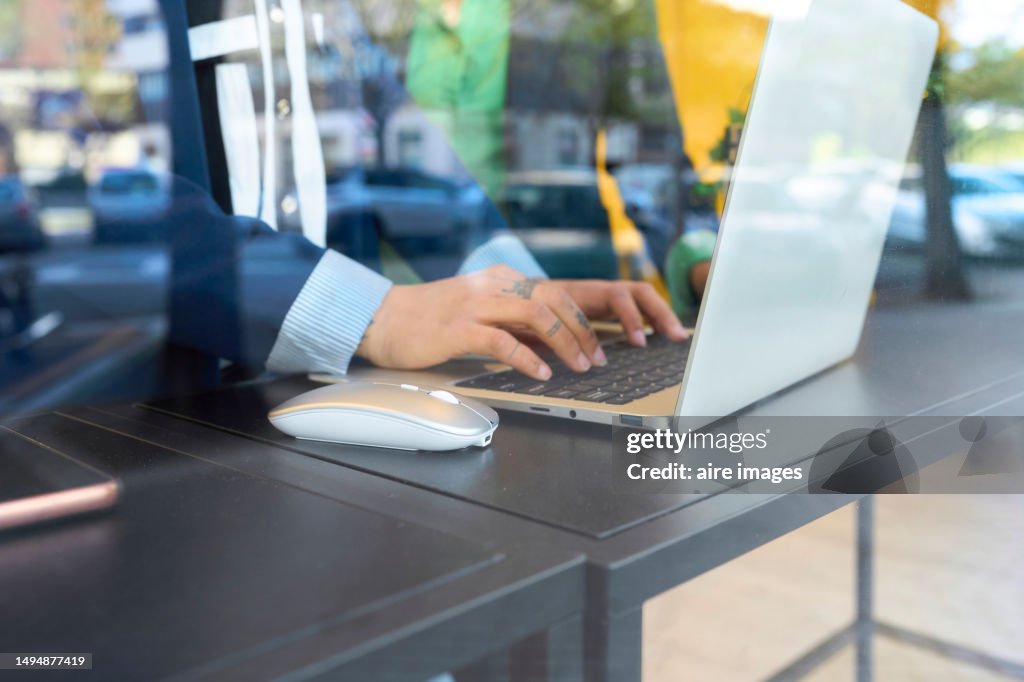 Closeup through glass of the hands of a woman sitting at a desk using a computer mouse, side view