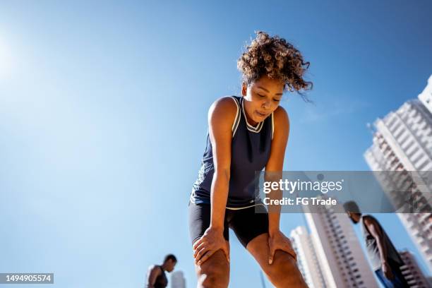 tired mid adult woman during exercises outdoors - hand on knee stock pictures, royalty-free photos & images