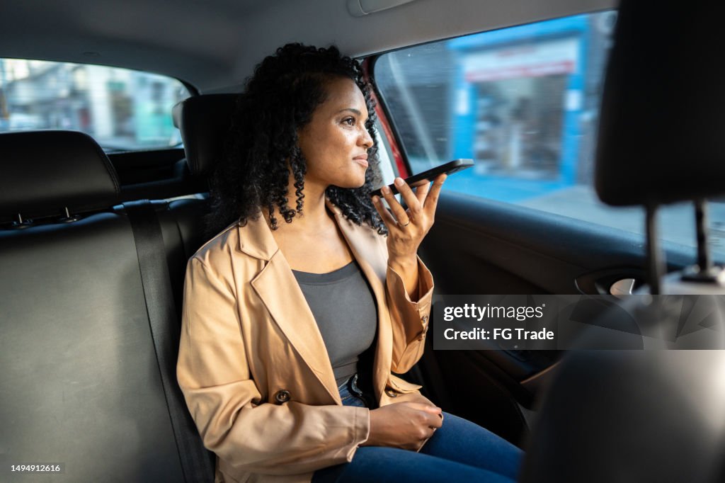 Mittlere erwachsene Frau, die eine Voicemail mit Mobiltelefon im Taxi sendet