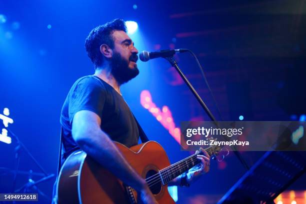 cantante masculino tocando la guitarra en el escenario - cantautor fotografías e imágenes de stock