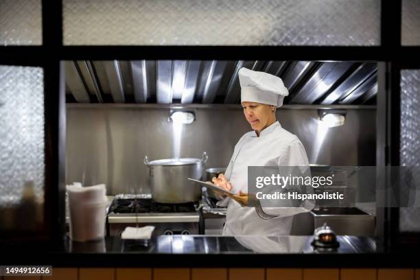 chef working at a restaurant and looking at a recipe on a tablet - chef taking notes in commercial kitchen stock pictures, royalty-free photos & images