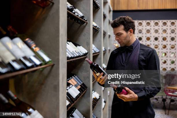 sommelier sélectionnant deux bouteilles de vin rouge dans une cave - cave à vin photos et images de collection