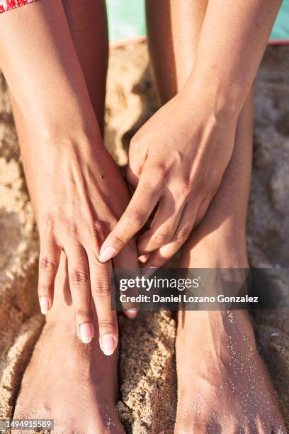 hands of a woman touching her feet on the beach - female feet stockfoto's en -beelden