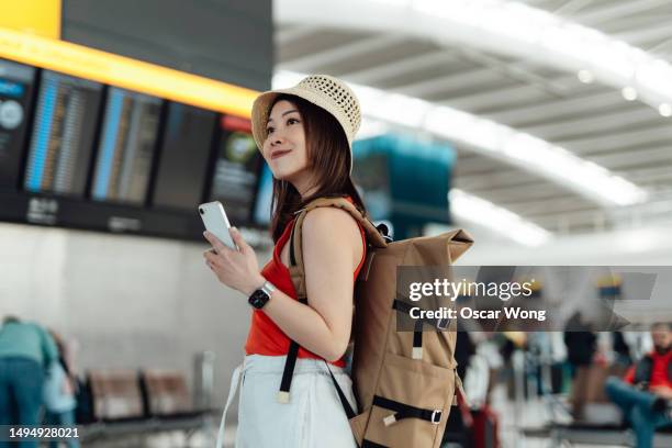 young asian woman with backpack using smartphone against arrival departure board at the airport - red stock pictures, royalty-free photos & images