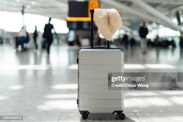 a hand luggage with a straw hat at the airport - lost luggage stock-fotos und bilder