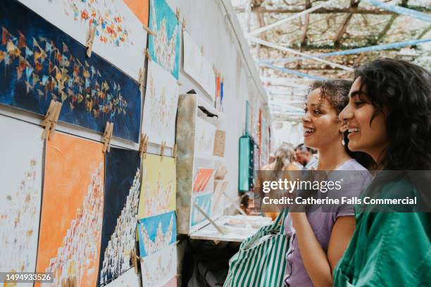 two woman browse art at an outdoor market stall - painting art product stock pictures, royalty-free photos & images