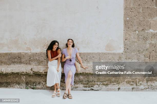 portrait of two beautiful young woman leaning against a rustic wall in italy - travel agent stock pictures, royalty-free photos & images