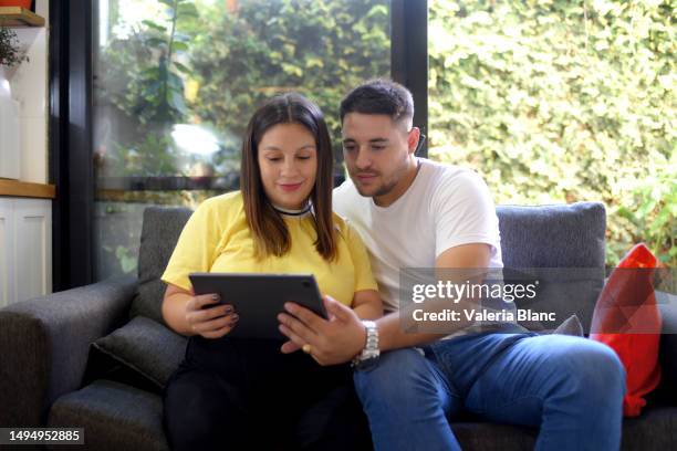 couple sitting on sofa using digital tablet - ipad blanc stock pictures, royalty-free photos & images