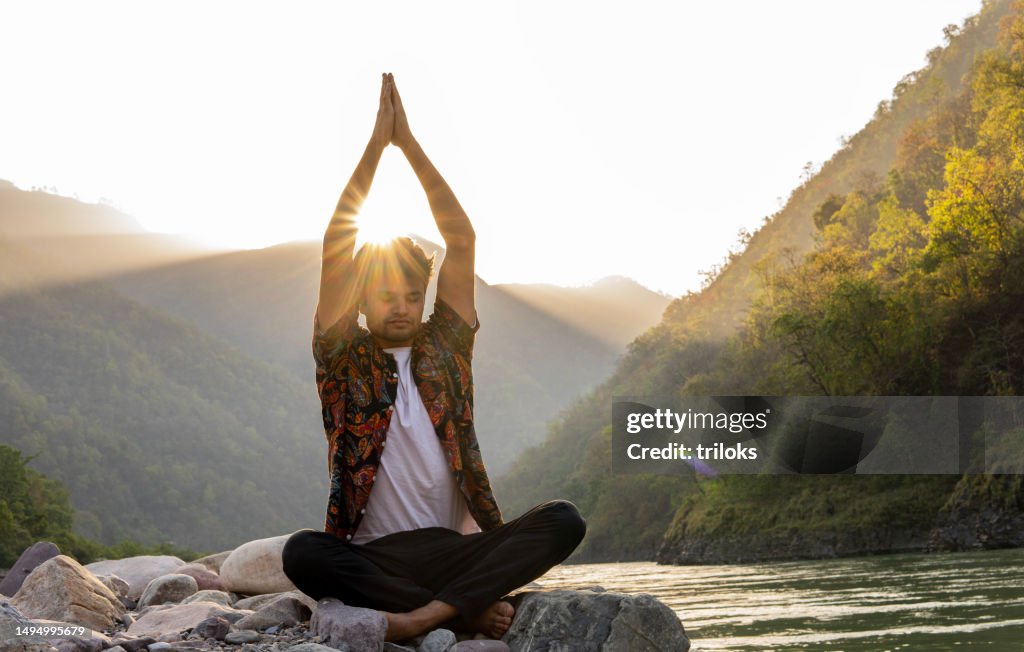 Young man meditating on rocks at lakeshore during vacation