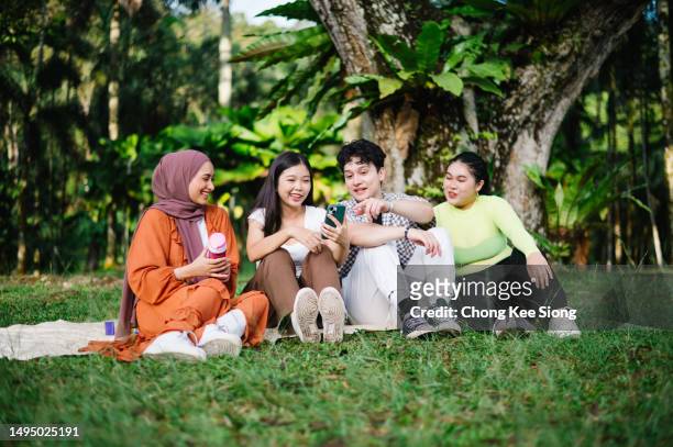 multiethnic friends having fun sitting on grass outdoor. - university student picnic stock pictures, royalty-free photos & images