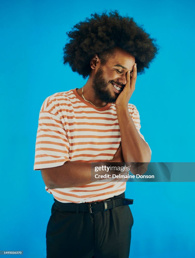 Junger schwarzer Mann mit Afro-Frisur, der sein Gesicht in der Hand hält und mit geschlossenen Augen lächelt. Stockfotografie