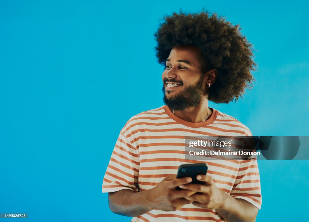 Stock image of a happy young black man looking away from the camera while holding his phone with copy space