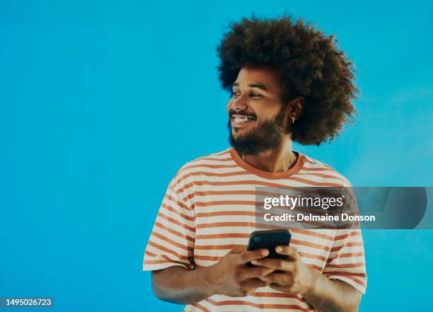 imagem de arquivo de um jovem negro feliz olhando para longe da câmera enquanto segura seu telefone com espaço de cópia - olhar de lado - fotografias e filmes do acervo
