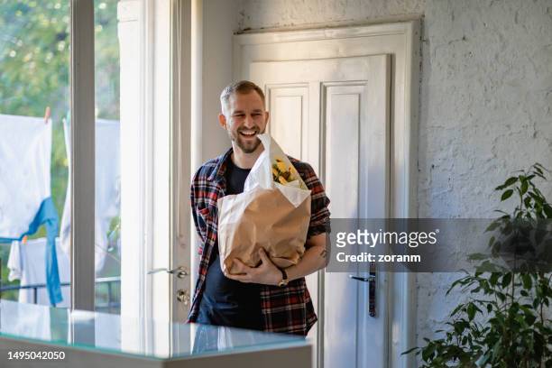 happy young man by the front door with paper bag delivered at home - entering shop stock pictures, royalty-free photos & images