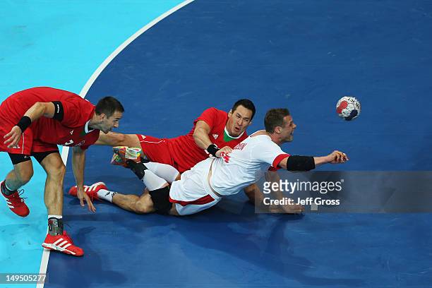 Michael Knudsen of Denmark is tackled by Ferenc Ilyes and Timuzsin Schuch of Hungary during the Men's Handball preliminaries group B match between...