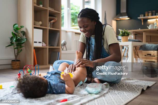 mother black ethnicity changing her baby boy diaper, during playtime - changing diaper stock pictures, royalty-free photos & images